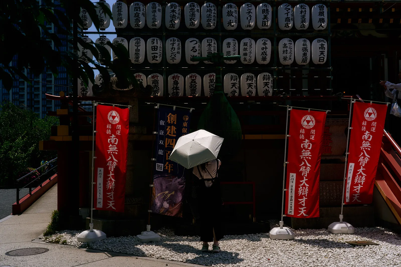 Photo of woman with white umbrella in front of a wall full of red japanese lanterns